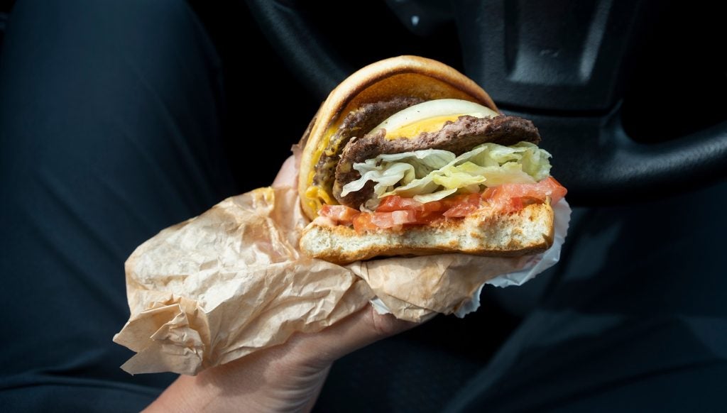 A person eats a double cheeseburger. So-called ‘forever chemicals’ are said to be found in fast-food wrappers.